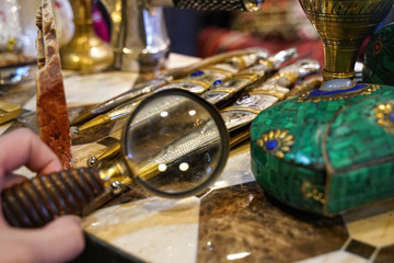 Examining details on traditional daggers through loupe magnifying glass in vintage antiques shop, close up detail