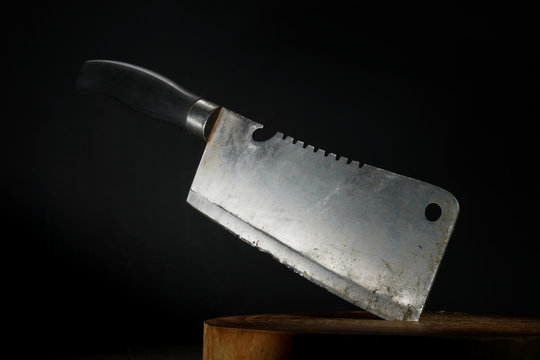 Old cleaver stuck on wooden cutting board with dark background
