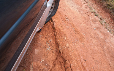 Driving 4wd vehicle on red dusty country road with big holes, detail on tire with low pressure going over rough terrain. Roads are in bad condition on Madagascar, especially after rain