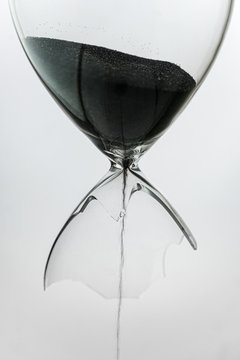 Broken sandglass with black sand leaking out