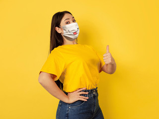 Pointing happy. Portrait of young caucasian woman with emotion on her protective face mask isolated...