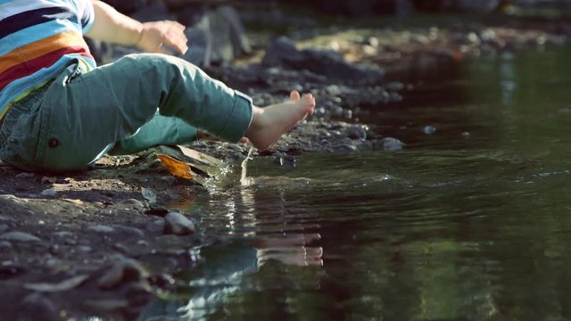 Close on toddler feet stepping into river then slipping and falling on bottom