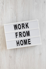 'Work from Home' words on a lightbox on a white wooden surface, top view. Overhead, from above, flat lay.