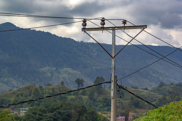 Home-made power pole with wires and old insulators against the backdrop of mountains and sky with...