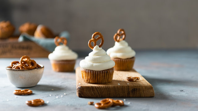 Sweet cupcakes with whipped cream and brezel on wooden board. Bakery, confectionery banner, cookbook recipe, menu. Side view, copy space