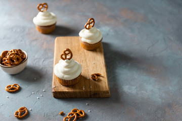 Sweet cupcakes with whipped cream and brezel on wooden board. Bakery, confectionery banner, cookbook recipe, menu. Side view, copy space
