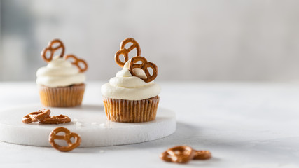 Sweet cupcakes with whipped cream and brezel on white marble tray. Bakery, confectionery banner, cookbook recipe, menu. Side view, copy space