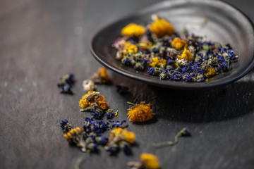 mixture of dry flowers for herbal tea styled studio shot on a black stone background in a black ceramic dish  © Lumistudio