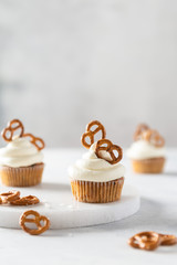 Tasty cupcakes with cream cheese decorated with brezel on wooden board on dark background. Party, happy birthday, pastry, bakery concept. Side view, copy space