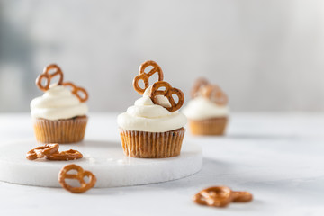 Tasty cupcakes with cream cheese decorated with brezel on white marble board on light background. Party, happy birthday, pastry, bakery concept