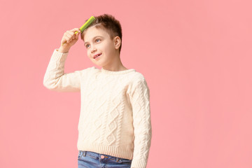 Little boy combing hair on color background