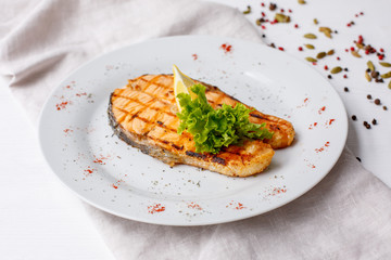 Grilled salmon steak served with lemon on a white plate