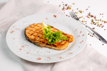Grilled salmon steak served with lemon on a white plate