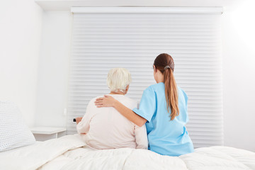 Pflegekraft hilft Seniorin im Pflegeheim vom Bett