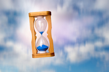 Sand clock in free fall on sky background. Concept: time flies very fast