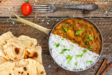 Chicken tikka masala spicy curry meat food served in copper pan with rice and fresh naan bread on vintage wooden background