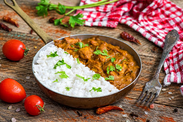 Chicken tikka masala spicy curry meat food served in copper pan with rice and tomatoes on vintage wooden background