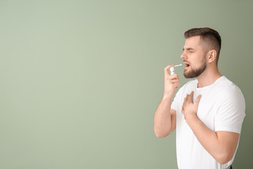 Ill young man with inhaler on color background