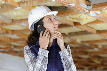 female builder using smartphone to communicate problem with ceiling