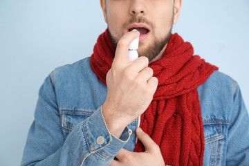 Ill young man with inhaler on color background