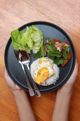 Hand served breakfast in the black round plate on the wooden floor. Fried egg rice and blend of fried chicken with lettuce.