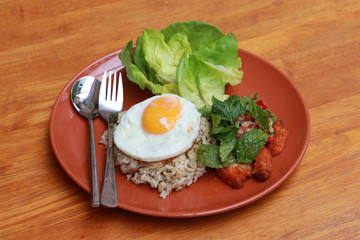 Breakfast in the dark orange color of round plate on the wooden floor. Fried egg brown rice and blend of fried chicken with lettuce.