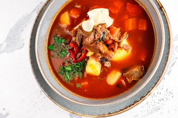 saturated spicy beef soup with vegetables and chili peppers on a gray plate on a white textured background close-up. top view.