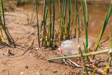 Dirty plastic bottle lying on the sand near the river. The concept of environmental conservation, ecology and earth day. Copy space
