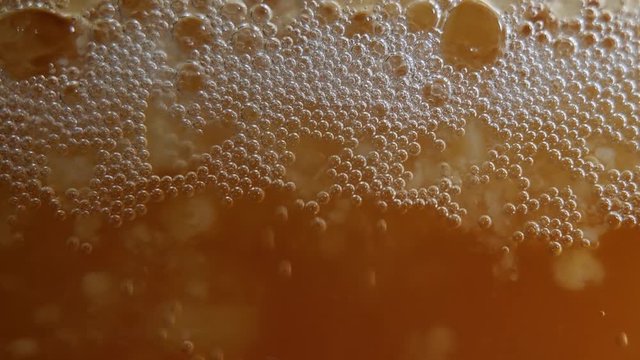 A locked off macro shot of yeast bubbles in active mead fermentation.