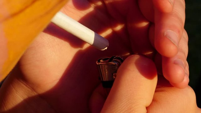 woman is lighting up a cigarette in the evening sun