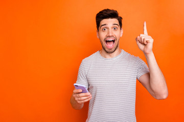 Photo of crazy millennial guy hold telephone hand raise index finger up have amazing creative blog post idea wear striped t-shirt isolated bright orange color background