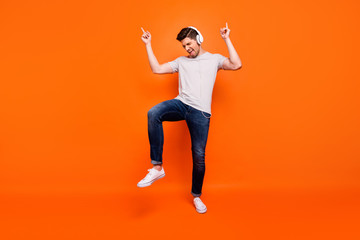 Fototapeta na wymiar Full body photo of funky cool guy cheerful party mood chilling listening earphones direct fingers up empty space wear striped t-shirt jeans shoes isolated bright orange color background