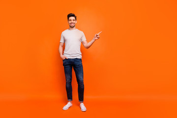 Full body photo of sales man guy cheerful person street casual look clothes directing finger empty space wear striped t-shirt jeans shoes isolated bright orange color background