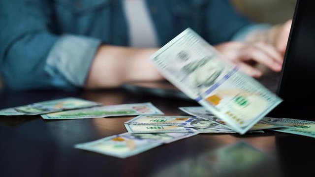 Hundred dollar bills falling on table of freelancer working on laptop