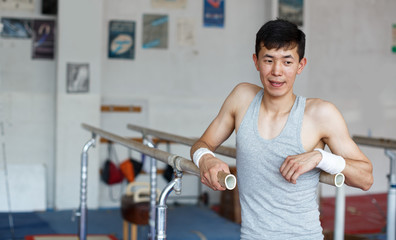 Smiling young male asian acrobat posing  at sport gym indoor