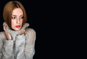 Portrait of a model girl in a sweater. young woman with brown hair posing on black background