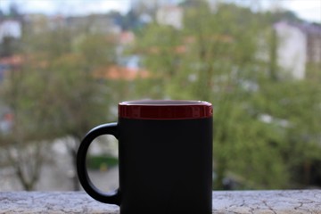 Red and black cup of caffe  with blurred trees and houses in the background