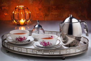 Vintage tea for two still with a stainless steel teapot, old Dutch teacups and sugar can on a tray in front of a rusty wall