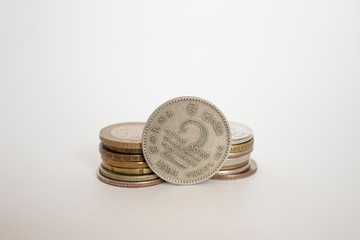 coin worth two rupees. a coin on a white background stands vertically in a row with other coins piled in a stack.