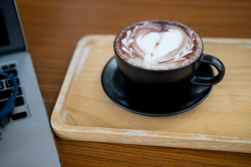 A cup of hot dark chocolate on wooden table with  laptop.