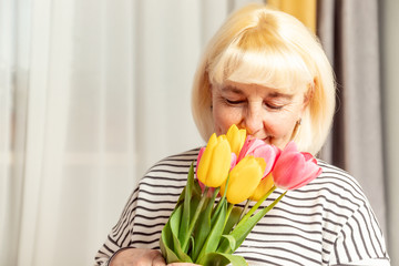 Happy mother's day. Adult blonde woman sniffing a bouquet of tulips flowers on a gray background