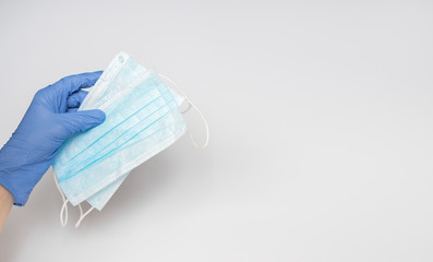 Hands of a caring doctor in blue medical gloves on a white background hold a two protective medical face masks, encouraging people to wear it during the period of quarantine, epidemic and pandemic