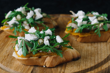 Italian appetizer - bruschetta with with arugula, parsley or cilantro, cheese and chicken on a wooden board