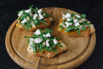 Italian appetizer - bruschetta with with arugula, parsley or cilantro, cheese and chicken on a wooden board