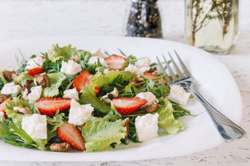 Light spring salad on a white background. Proper nutrition. Diet. Proper nutrition. Diet. Slat with greens, strawberries and cheese