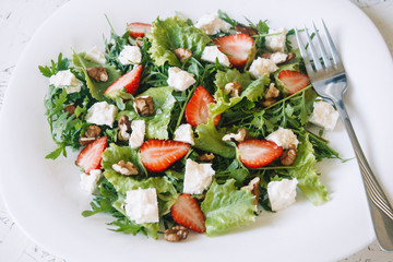 Light spring salad on a white background. Proper nutrition. Diet. Proper nutrition. Diet. Slat with greens, strawberries and cheese