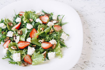 Light spring salad on a white background. Proper nutrition. Diet. Proper nutrition. Diet. Slat with greens, strawberries and cheese