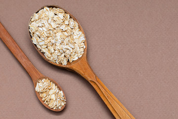 oat flakes in a two wooden spoon on a brown background