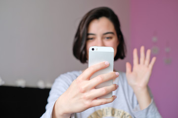 A woman smiling and waving to her phone video chatting with loved ones