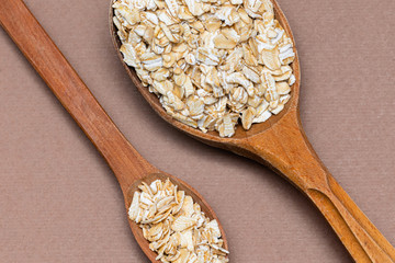 oat flakes in a two wooden spoon on a brown background